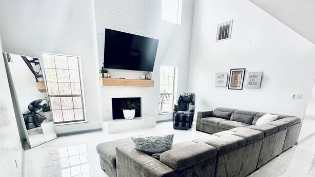 A modern living room with a large sectional sofa, a flat-screen TV mounted above a fireplace, and a minimalist decor style.