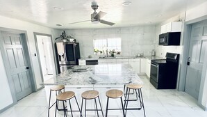 A modern kitchen with a large island, bar stools, stainless steel appliances, and a ceiling fan.
