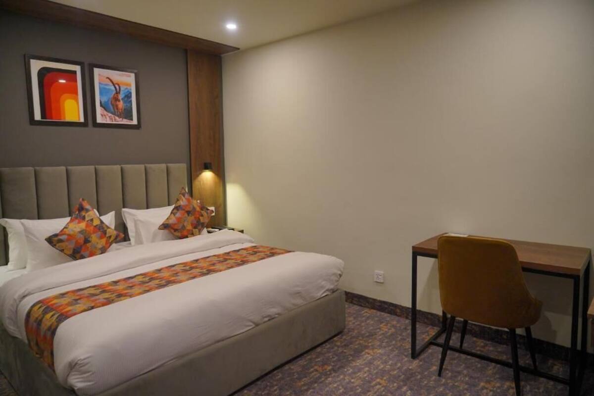A hotel room with a bed, a desk, and two framed pictures on the wall.