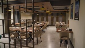A dining area with multiple tables and chairs, a kitchen area in the background, and pendant lighting. - Destination Hotel Gilgit (Gilgit)