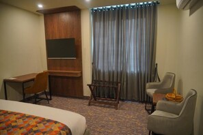 A hotel room with a bed, a desk, two chairs, a small table, and a curtain.