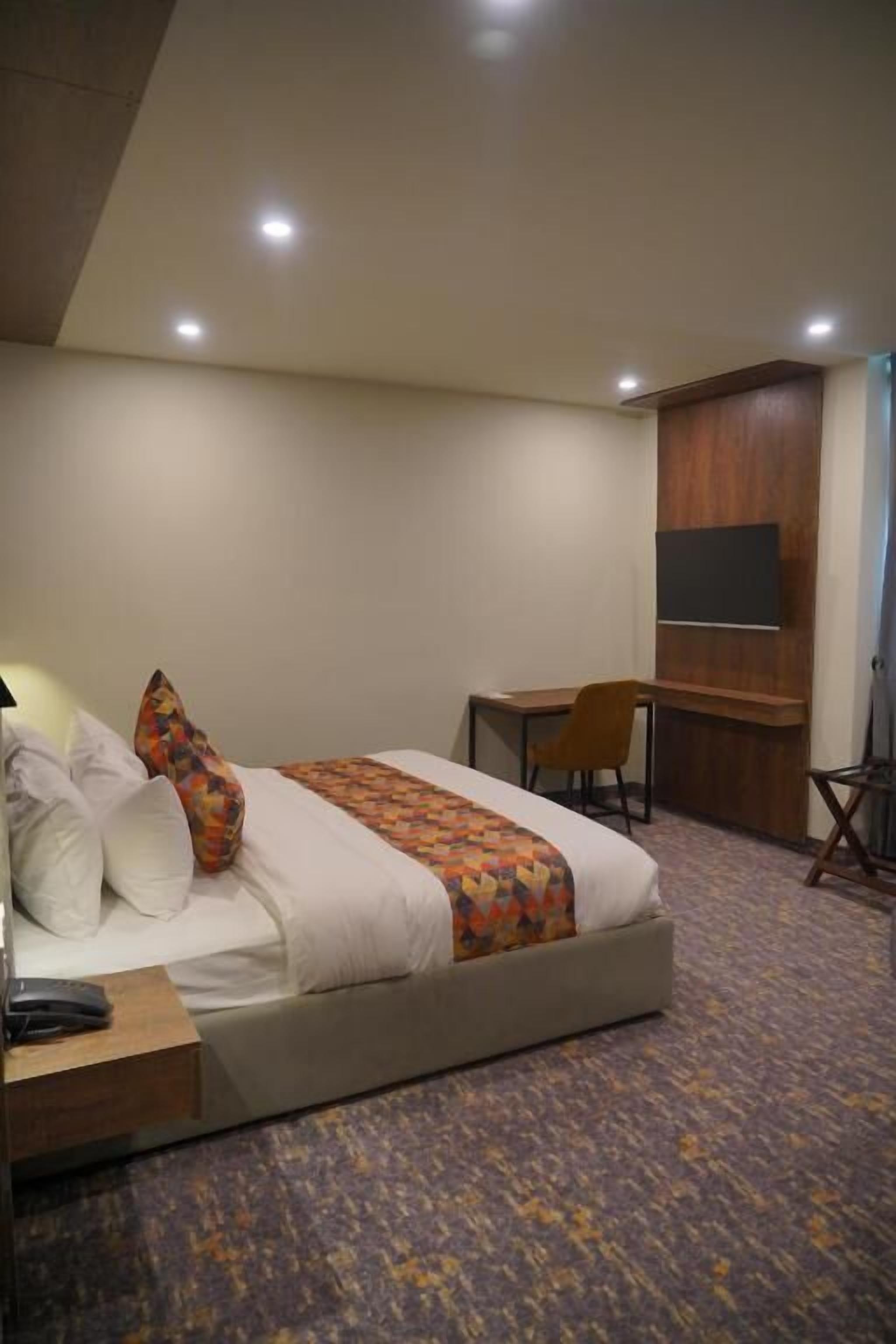 Habitación de hotel con cama, escritorio, silla, televisor montado en la pared y piso alfombrado.