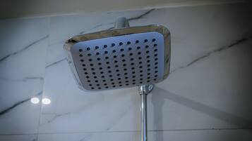A showerhead with a square design and multiple holes, mounted on a metal pole, against a tiled wall.