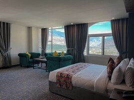 Habitación de hotel con una cama grande, dos sillones, una mesita y vistas a las montañas a través de la ventana.