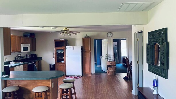 Une cuisine dotée de meubles en bois, d’un four à micro-ondes, d’un réfrigérateur, d’un coin bar avec des tabourets et d’un ventilateur de plafond.