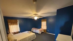 Une chambre d’hôtel avec deux lits, un ventilateur de plafond et une petite table.