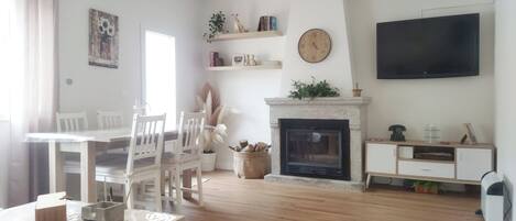 A living room with a fireplace, a television, and a dining area with chairs and a table.