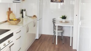 A compact kitchen with white cabinets, a microwave, a refrigerator, a dining table with two chairs, and a small potted plant.