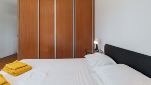 Een slaapkamer met een bed, witte lakens, een houten garderobe en een bedlampje.