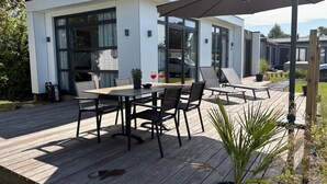Un patio moderno al aire libre con terraza de madera, mesa y sillas, y un paraguas grande.