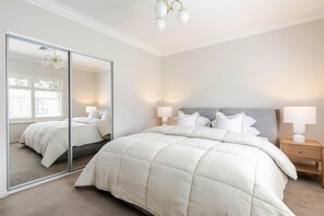 Camera da letto con un ampio specchio, un letto con biancheria da letto bianca, due comodini con lampade e un lampadario.