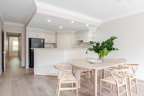 Una cucina moderna con mobili bianchi, un'isola centrale e un'area pranzo con sedie e tavolo in legno.