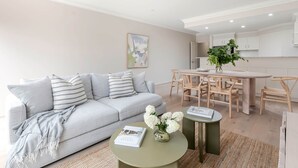 A modern living room with a grey sofa, a round coffee table with a book and flowers, and a dining area with wooden chairs and a table. - Adelaide Oval Townhouse / Walk to the AFL & CBD (North Adelaide)