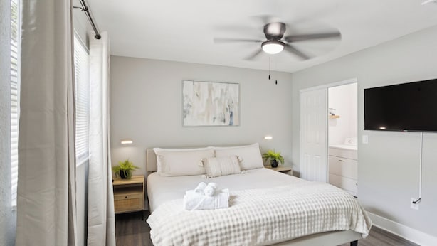 Un dormitorio moderno con una cama, mesitas de noche, ventilador de techo y televisor montado.
