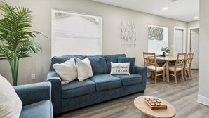 Una sala de estar con un sofá azul, una mesa de centro y una zona de comedor con una mesa y sillas de madera.
