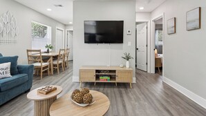 Una sala de estar moderna con una televisión de pantalla plana, un comedor con muebles de madera y un sofá azul.