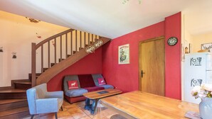Een woonkamer met een houten trap, een bank, een bijzettafeltje en een koelkast.