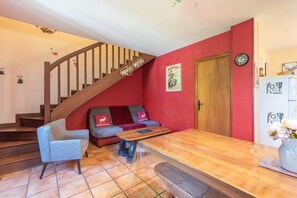 Una sala de estar con escalera de madera, sofá, una mesa de centro y un refrigerador.