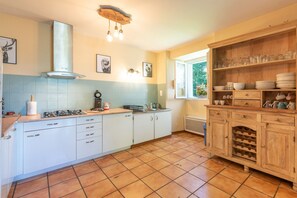 Une cuisine avec des meubles blancs, une cuisinière à gaz, un porte-bouteilles à vin en bois et une fenêtre donnant sur un paysage verdoyant.