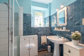 Une salle de bain avec une douche, un lavabo, un miroir et des plantes en pot.