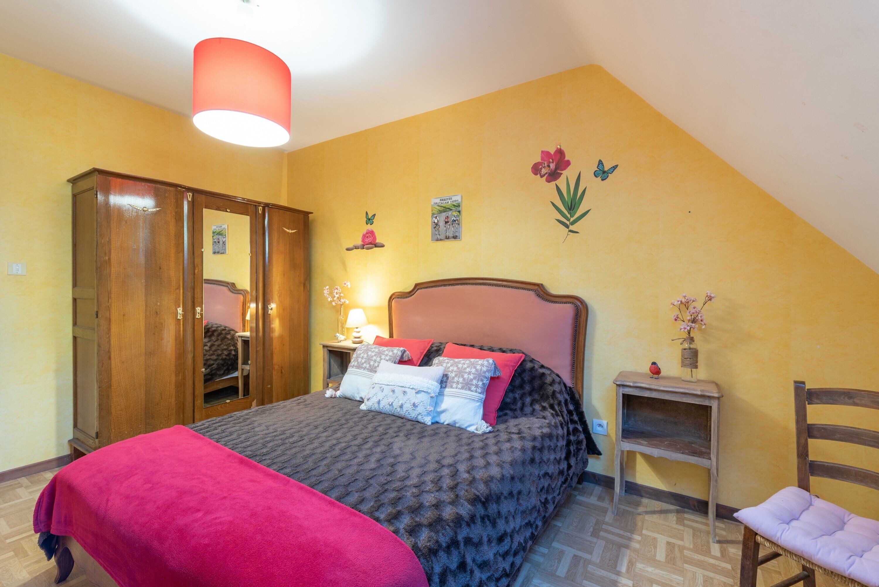 A bedroom with a bed, a wardrobe, a bedside table with a lamp, a chair, and wall decorations.