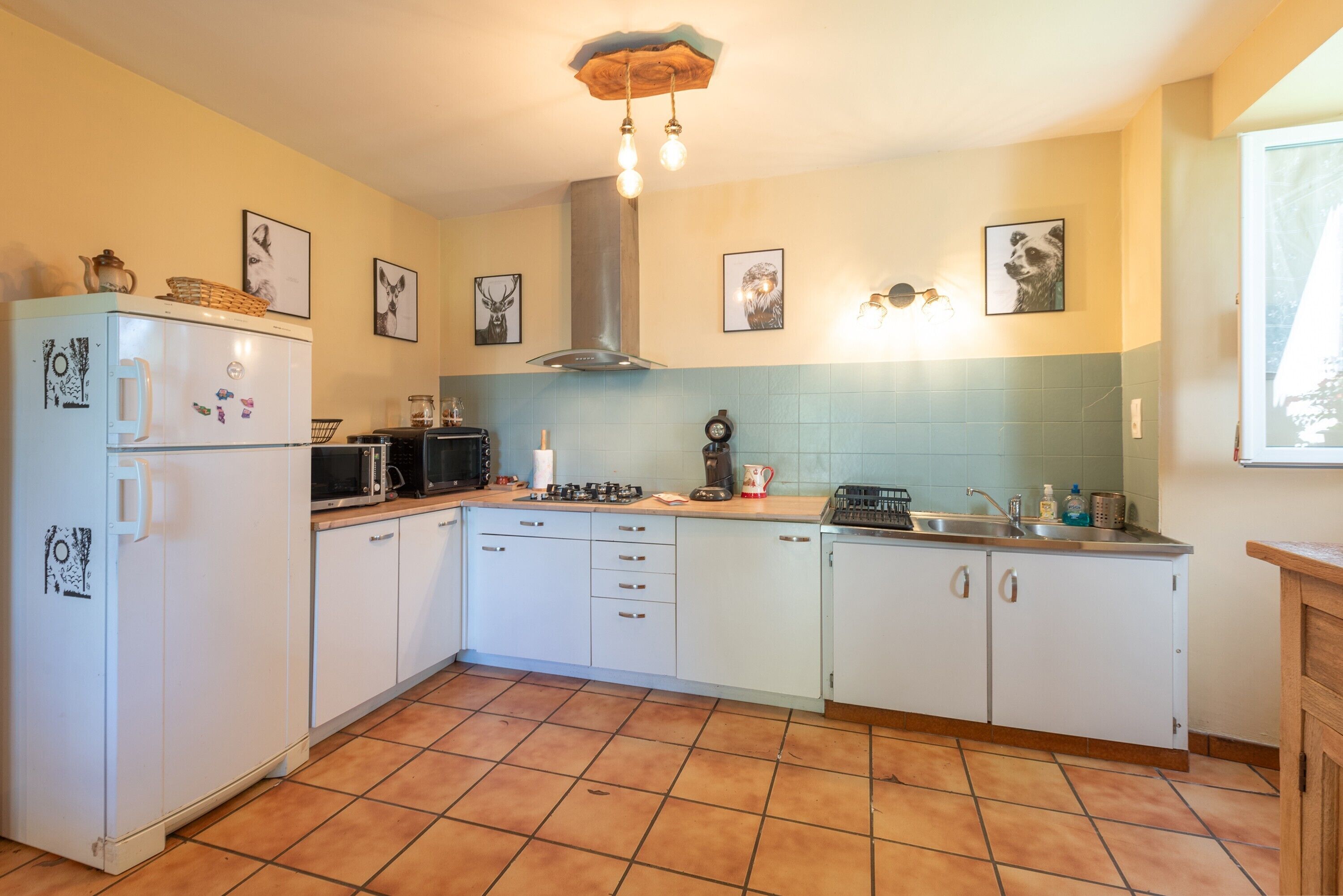 A kitchen with white cabinets, a stove, a sink, and a refrigerator. There are framed pictures on the walls and a ceiling light fixture.