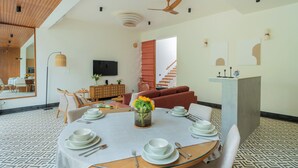 A modern living room with a dining area, a TV, and a staircase. - ELIVAAS Mirai Tauras 3BHK (Vagator)