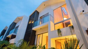 A modern multi-story building with large windows and balconies, surrounded by greenery. - ELIVAAS Mirai Tauras 3BHK (Vagator)