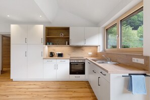 Een moderne keuken met witte kasten, een inbouwoven, een spoelbak en een raam met uitzicht op groen.