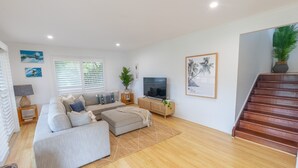 A spacious living room with a large grey sofa, a TV, and a staircase leading to another level.