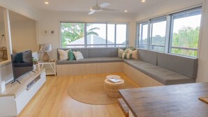 A modern living room with a large window, a ceiling fan, and a flat-screen TV on a wooden stand.