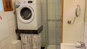 Une petite salle de bain équipée d’un lave-linge, d’une douche à parois de verre et d’un lavabo.