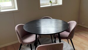 Une pièce avec une table ronde, quatre chaises, une petite plante en pot et deux fenêtres.