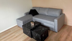 Un canapé d’angle gris avec un coussin noir, une table basse en marbre noir et un petit vase décoratif.