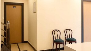 A hotel lobby with a reception desk, two chairs with green cushions, a wooden door labeled '101', and a ceiling fan. - Hari Niwaas Guest House by VM Stays (Varanasi)