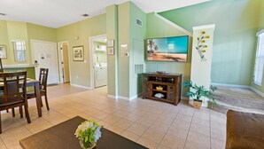 A living room with a TV, a dining area with chairs, and a kitchen area with a washing machine. - Ccl8538 (Kissimmee)