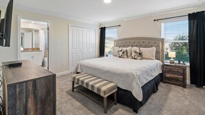 A bedroom with a large bed, a bench, a TV, and a window with curtains.