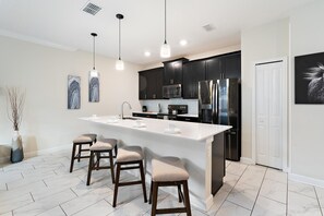 Une cuisine moderne dotée d’un îlot central, de meubles de couleur sombre, d’appareils électroménagers en acier inoxydable et de luminaires suspendus.