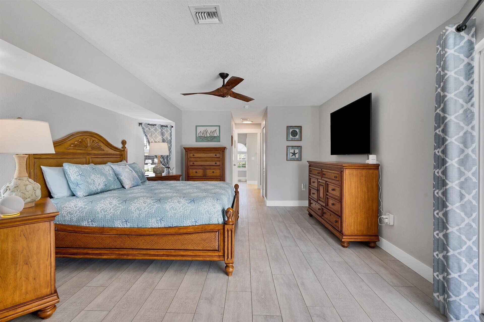 A bedroom with a wooden bed, a ceiling fan, a dresser, and a television.