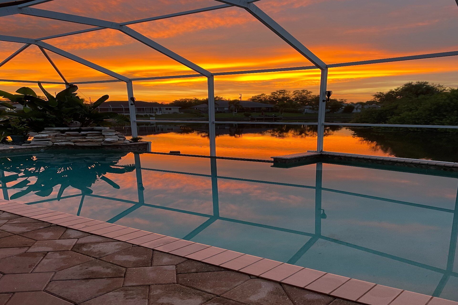 Una piscina exterior con vista despejada a la puesta de sol sobre una masa de agua, rodeada por una estructura metálica y escalones de piedra.
