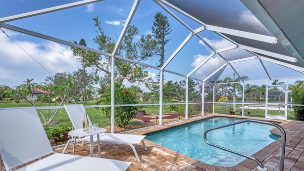 A covered outdoor swimming pool with white lounge chairs and a clear view of the surrounding landscape. - Cod917 (Punta Gorda)