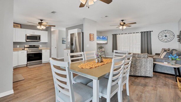 A modern kitchen with white cabinets, a stainless steel refrigerator, and a microwave. There is a dining area with a wooden table and white chairs. - Dbd1014 (Port Charlotte)