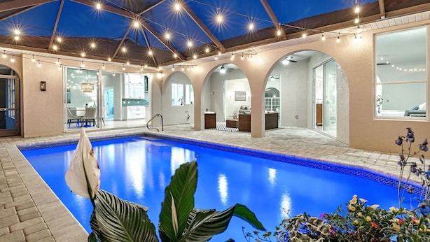An indoor swimming pool with a clear blue water feature, surrounded by a covered patio area with seating and a view of the interior space.