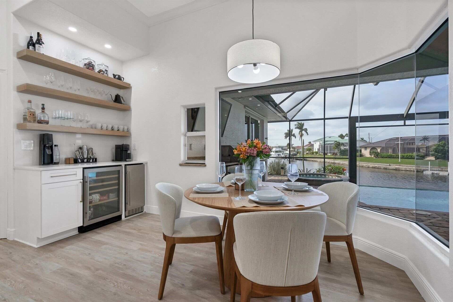 A modern dining area with a large window, a round table set for four, and a kitchen with open shelving.
