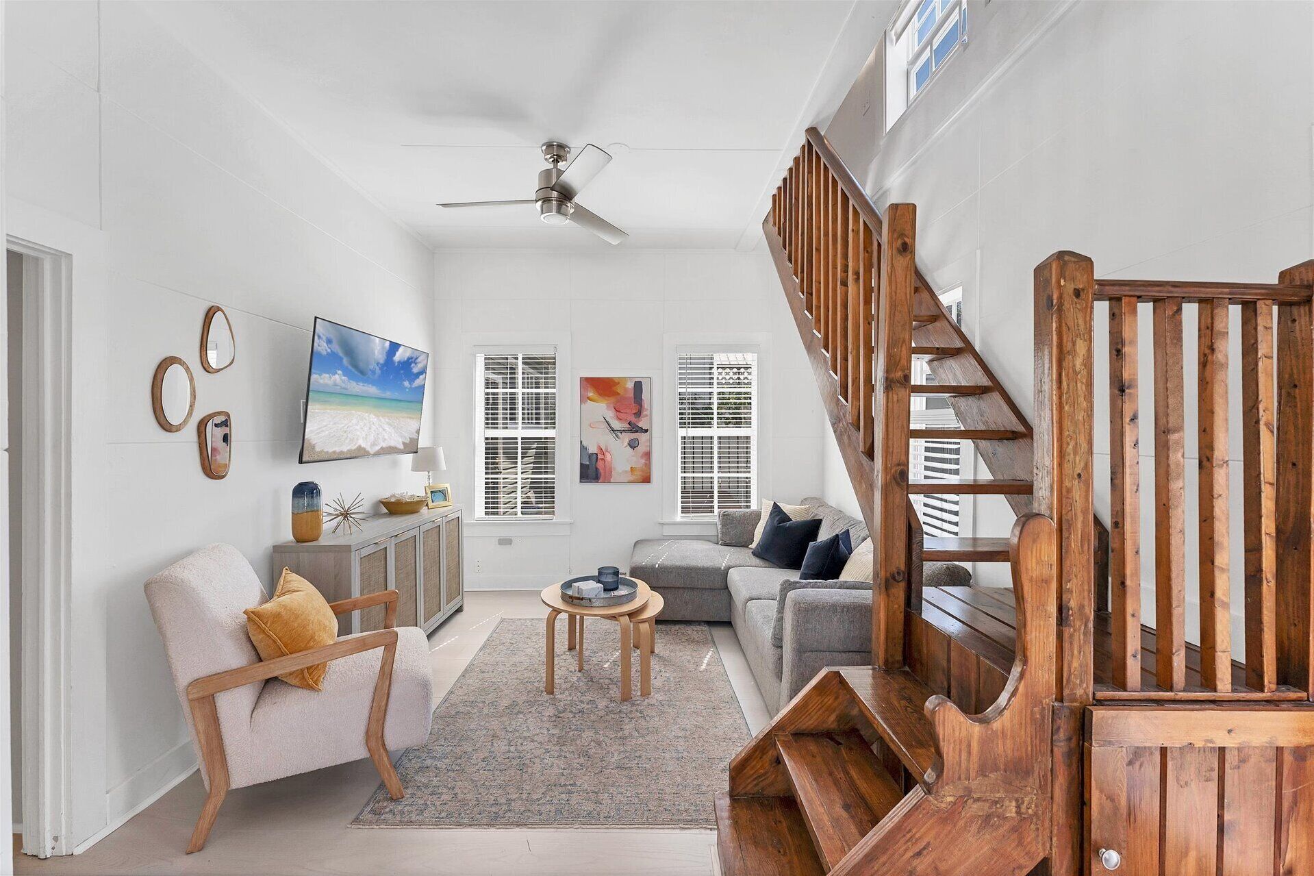 A spacious living room with a wooden staircase, a ceiling fan, and a large window.