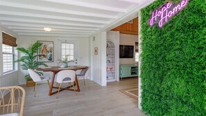 A dining area with a wooden table and chairs, a green wall with a neon sign, and a large plant. - HH123 Summary:<br>Welcom (Clermont)