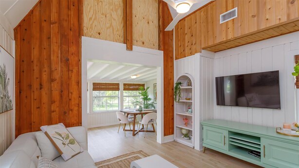 A spacious living room with a wooden ceiling, a white sofa, a dining area with a table and chairs, and a television mounted on the wall. - HH123 Summary:<br>Welcom (Clermont)