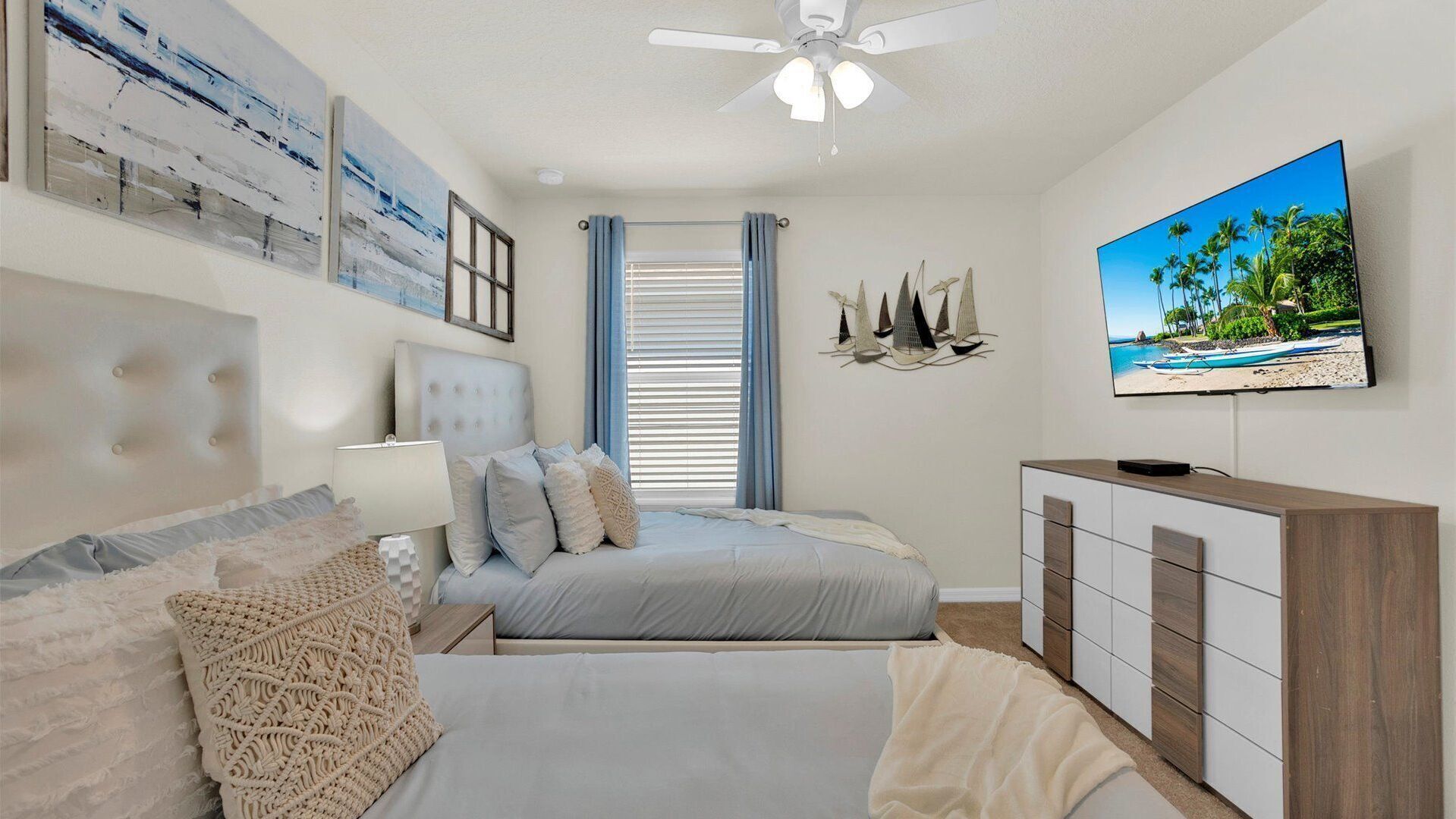 Um quarto com uma cama, televisão, ventilador de teto e obras de arte nas paredes.