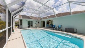 An indoor swimming pool with clear water, surrounded by lounge chairs and a covered patio area.