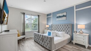 A bedroom with a large bed, two bedside tables, a nightstand, a desk, and a window with blinds. - Cvt1749 (Kissimmee)